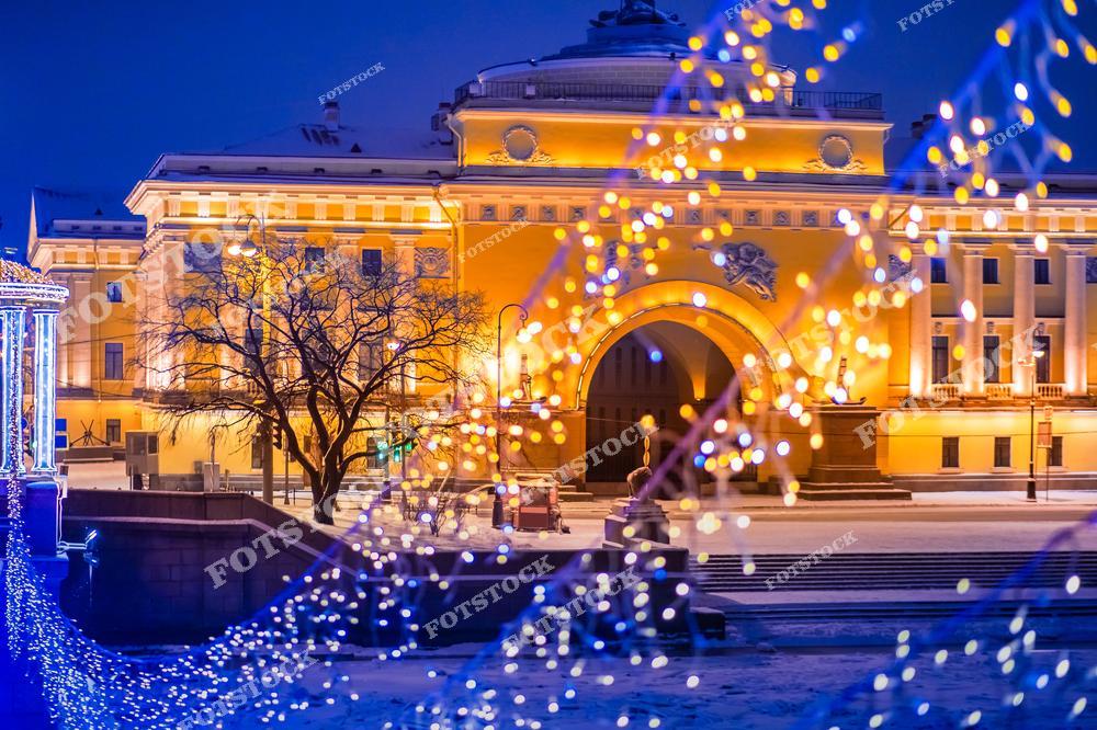 На снимке изображено Адмиралтейство, одна из главных достопримечательностей Санкт-Петербурга, украшенное рождественской иллюминацией. Гирлянды создают праздничное настроение, гармонично дополняя архитектурный ансамбль здания. Вечерний свет и зимняя атмосфера подчеркивают красоту исторического центра города. Это место, где рождается ощущение волшебства и уюта.